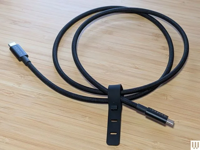 Cable USB-C trenzado negro enrollado sobre una superficie de madera.