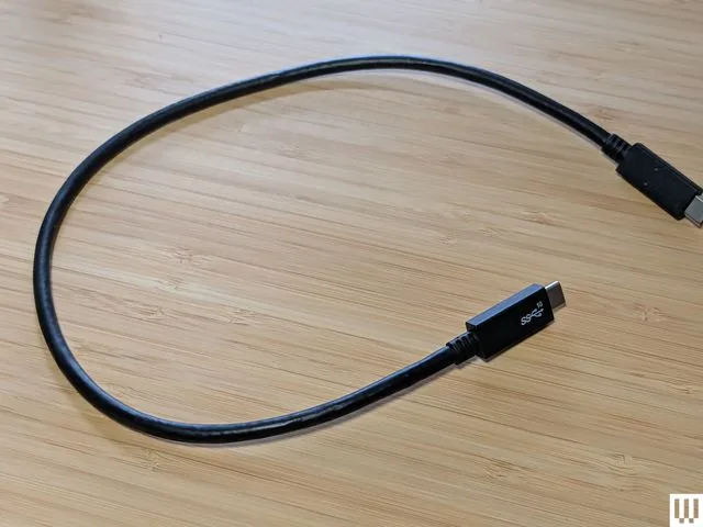 Un cable negro con conectores USB-C sobre una superficie de madera.